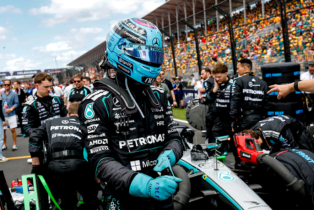 Formula 1 driver sitting in the race car on the starting grid with team and spectators.